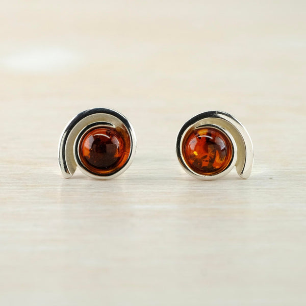 Round pieces of amber, with darker internal markings are set in a silver frame thatcircles around itself, looking a little like an eye.