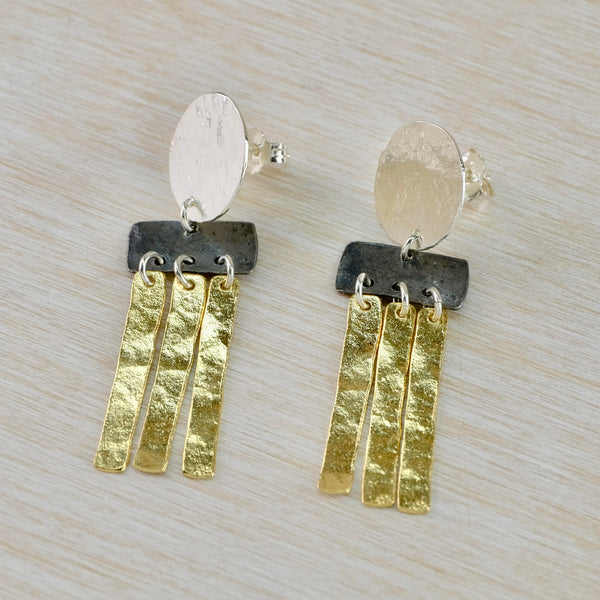 Earrings in three sections. The top one is a bright textured silver  flat round disc . Below this  a horizontal dark grey rectangle, slightly wider than the disc. Then three gold textured vertical long rectangles attached to the  horizontal one by silver rings. These are about twice as long as the  darker one is wide.