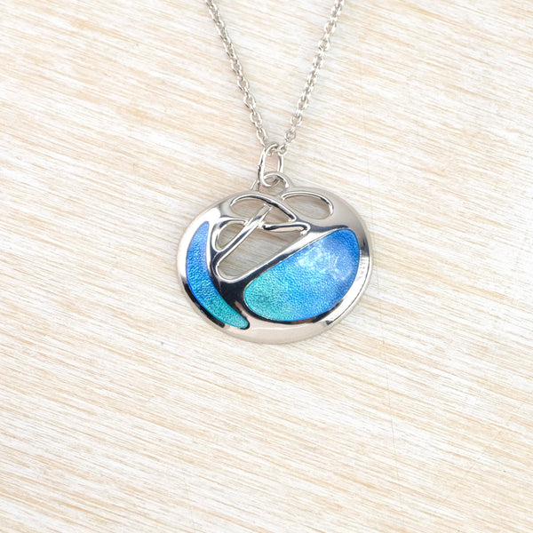 The overall pendant is a slighty flattened circle . There are two panels of blue/green enamel, one narrow curve to the left and a wider more horizontal shape to the bottom right. The middle top is polished silver in a vague  celtic design.