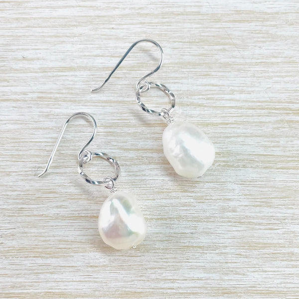 Irregular shaped, almost teardrop, glossy pearls hang below silver rings which have been twisted round on themselves. The rings are slightly smaller than the pearls and hang from a silver hook.