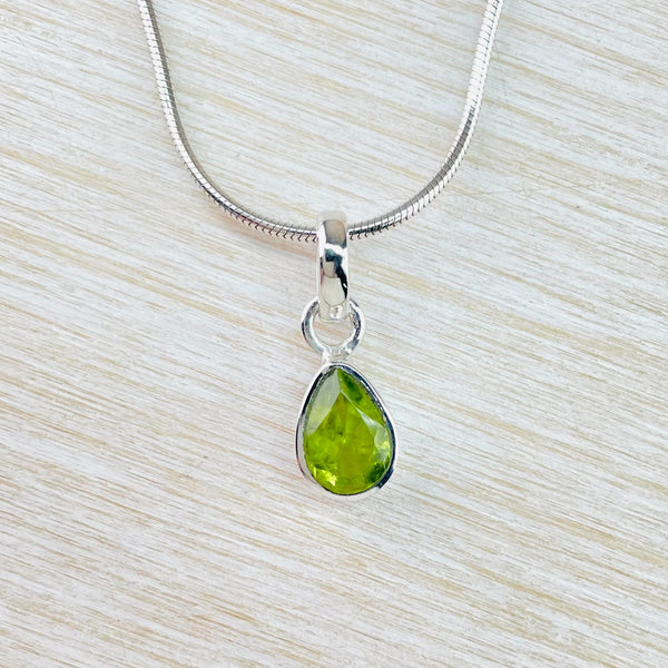 Bright light lime green stone which has been faceted is set in a silver teardrop frame. Joined to a silver ring at the top, then a plain bale with a silver chain thread through.