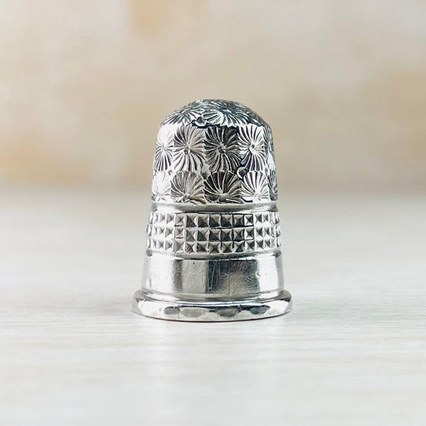 The thimble is split into three different design sections. The top third is a repeated floral design, then there is three rows of squares - indented, then a plain high polished section.