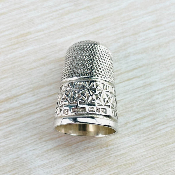 silver thimble with two different designs in two halves. The top is lots of little dots, the bottom is larger flower design. each with 9 pegtals. Their is a plain silver band around the bottom. 