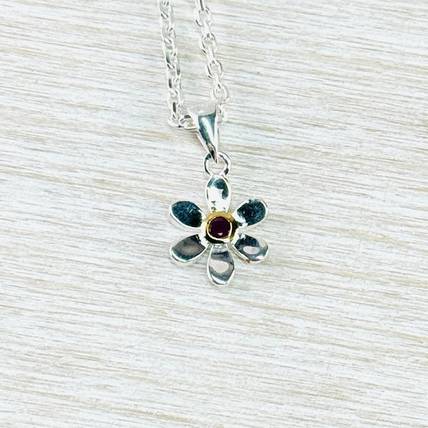 Six petalled silver flower with a deep red ruby stone in the centre. The stone is surrounded by gold . A very delicate pendant hanging off  asilver link chain.