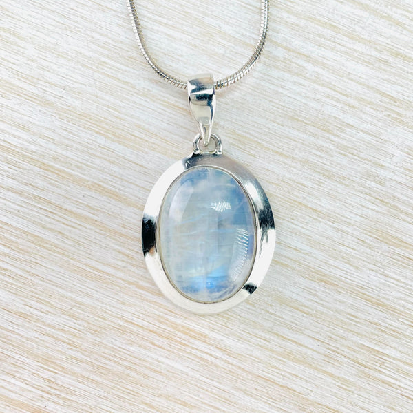Pretty grey with bright blue flecks oval stone is set in a very shiny plain silver frame. Hangs off a simple bale on a chain. 