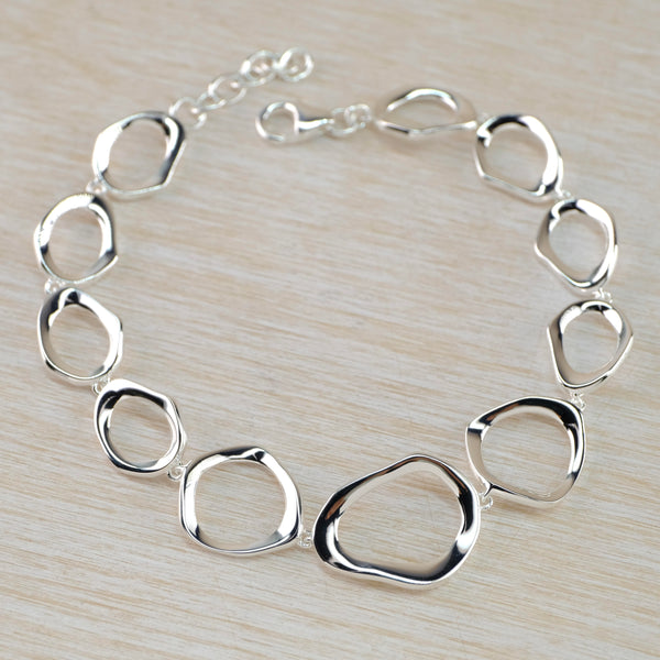 A full bracelet comprised of outline pebble shaped polished silver links. They are different shapes getting smaller as they go further back. There is a short chain at the back and a lobster catch. 11 links in total