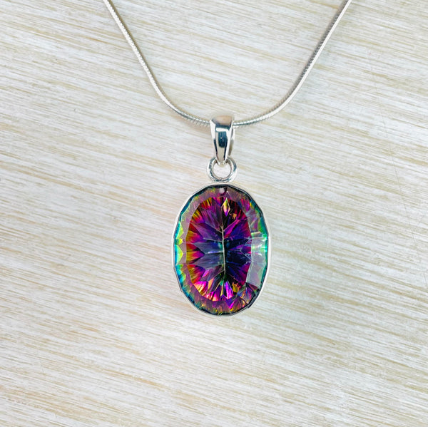 Oval mystic topaz stone is faceted showing pink/purple and green colours. Set in a silver frame and hanging from a simple round silver bale.