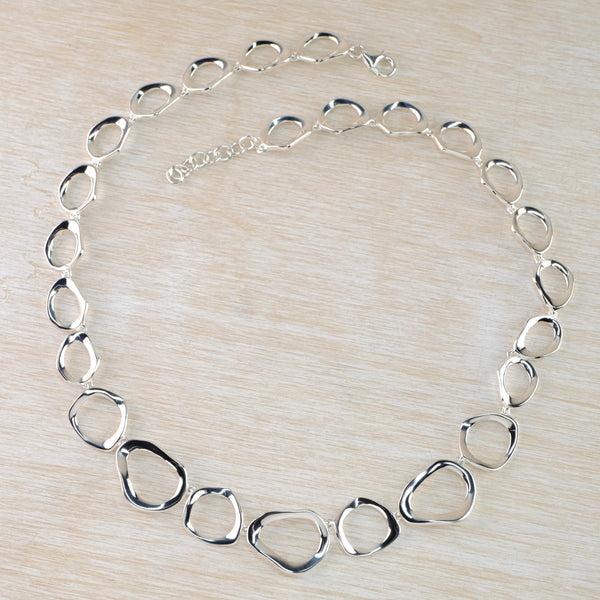 A full necklace comprised of outline pebble shaped polished silver links. They are different shapes getting smaller as they go further back. There is a short chain at the back and a lobster catch. 25 links in total