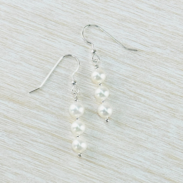 Three round glossy pearl beads, seperated by tiny silver spacers, hang off a silver hook.