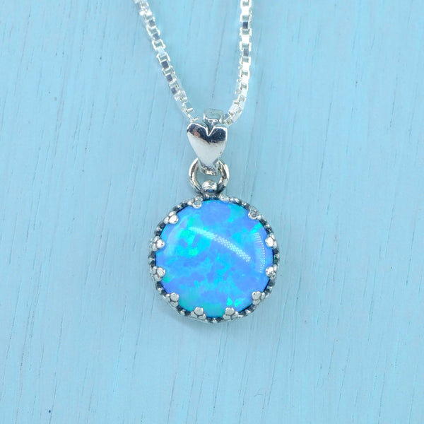 Bright blue/green opal stone is set in a round silver surround with 12 little decorative 'teeth' around the rim. At the top a circular silver ring threads through a little heart which the chain threads through. 