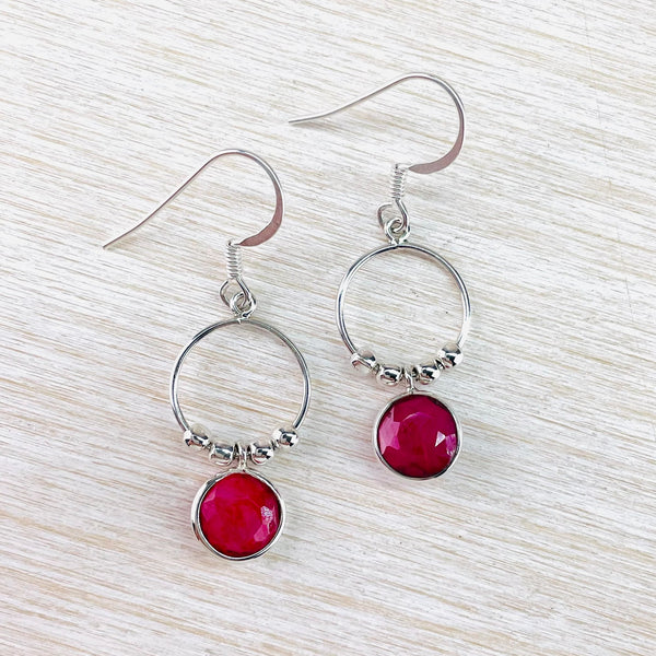 Deep pink red opaque stones. Round stones set in silver hang below a silver circle, twice the size of the stone and facing front. At the bottom of the circle are four silver beads, two on each side of the stone. The earrings have a silver hook.