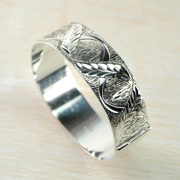 Shiny wide silver bangle with a double helix design on a textured background on the front half. One trand of the helix is plain the other has a leaf design .