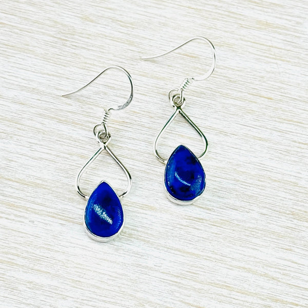 A teardrop shaped stone , set in silver, sits below an open teardrop silver shape, slightly protruding into the shape creating a heart shape. The stone is a smooth finish navy blue.
