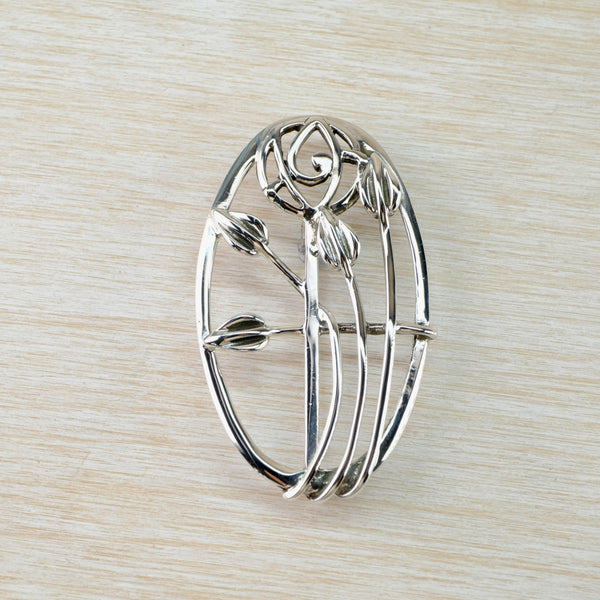 A n oval sterling silver brooch with a round detail featuring a floral design, inspired by Charles Rennie Mackintosh's work.