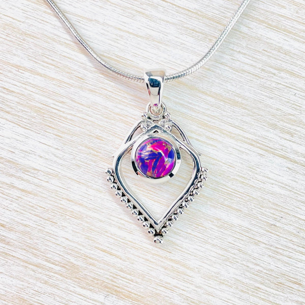 Overall diamond shape hanging from  a silver hook. At the top of the diamond the silver is crossed over to join the hook.  Below  this a round bright blue and purple  turquoise stones, set in silver, are set centrally but a little above the half way point length wise. The bottom half of rhe diamond has tiny silver balls along the outside. Hanging from a silver chain.