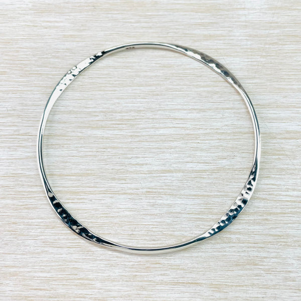 A round silver bangle which has 8 sections. Every other section has been flattened and hammered, the remaining sections are round and polished,
