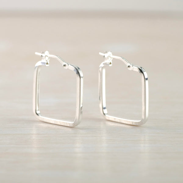 Shiny silver square shaped hoops. The shape of the wire forming the earring  is square. At the top is a slightly curved wire that clicks into a 'u'shaped clip.