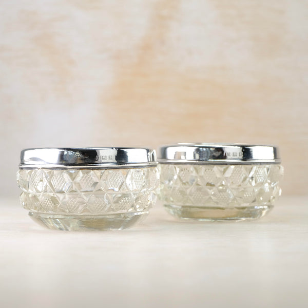 Small cut glass bowls are topped with a bright shiny silver rim, about a quarter the size of the bowl. The glass is cut with two rows of X markings with a diamond shape of little dots between each cross.