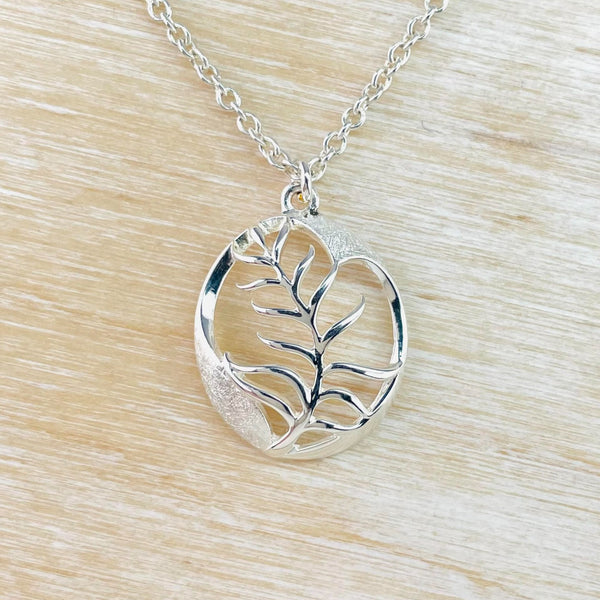 Oval shaped silver pendant with matt finish panels top and bottom. In the muddle is a high polished silver sprig, lwith a ferny look.