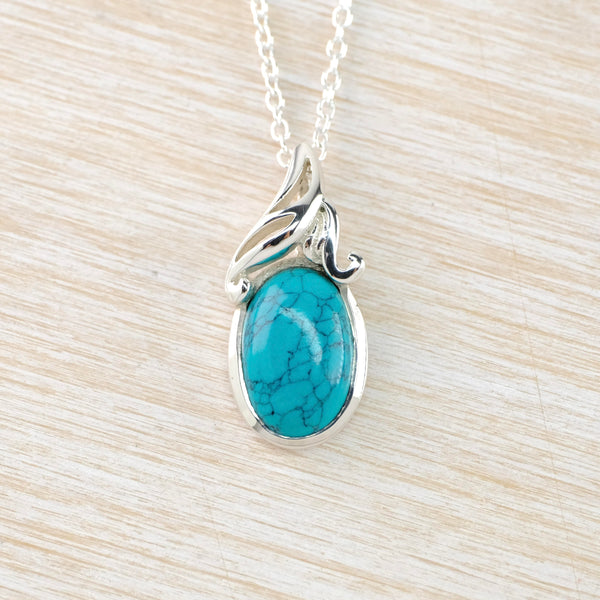 An oval turquoise stone with lots of crackle markings is set in shiny silver. At the top, silver has been twisted, like a scribble  and polished .