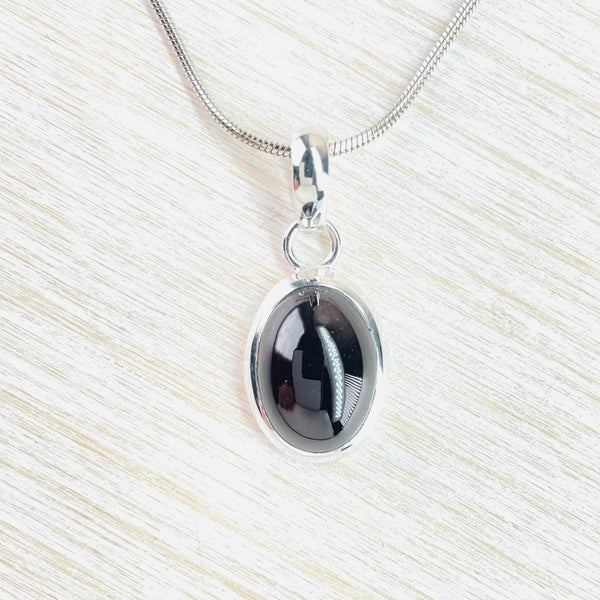 Very simple deep red smooth garnet, oval in shape is set in silver. Attached to a round silver ring - set to face us - and an oval silver bale.