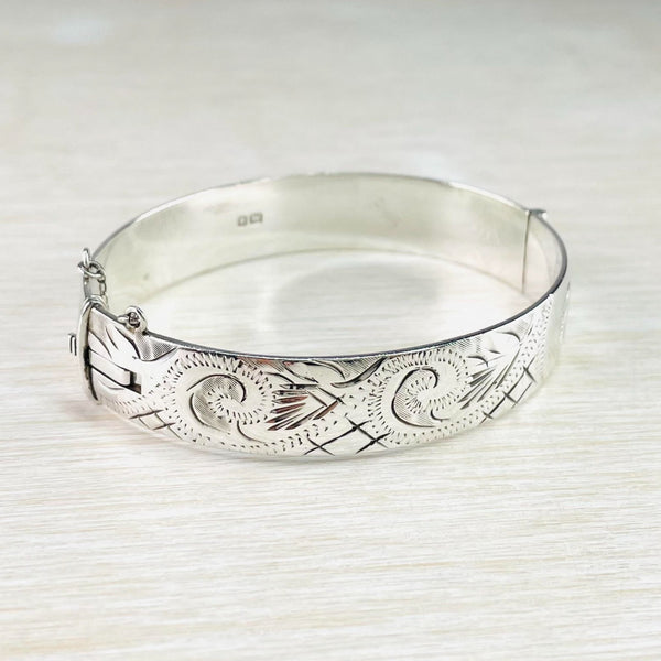 Oval bright silver bangle with a mix of swirls - formed with dots and dashes- and grids and leafy shapes. The hallmark is on show on the inside.