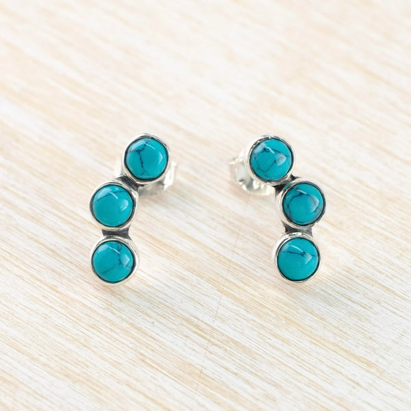 Three bright turquoise round stones, each set in silver, are set one below the other in a gentle curve.