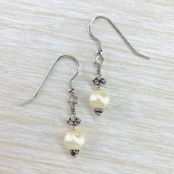 Lovely glossy cream coloured round pearls hang below a spot patterned silver bead. At the bottom of the pearl is a small similar bead and they hang from a silver hook.
