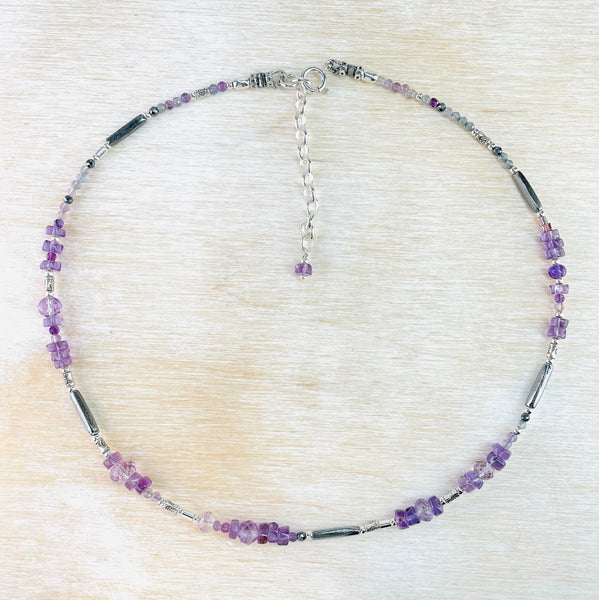 Groups of amethyst beads in different shades of purple and in different shapes and sizes are mixed with silver beads, some tubes, some balls around the length of the necklace.
