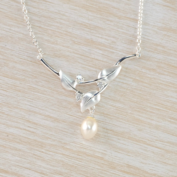 A Y shaped pendant with a glossy cream pearl dangling from the bottom. Three satin silver leaf shapes , intertwined with three little sparkly clear stones form the  Y shape. It hangs off a fine link chain.