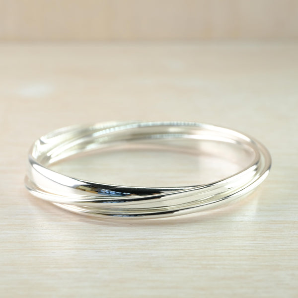 Three lovely shiny plain silver bangles, each a slightly different width, are intertwined together to look like one. They are round in shape.