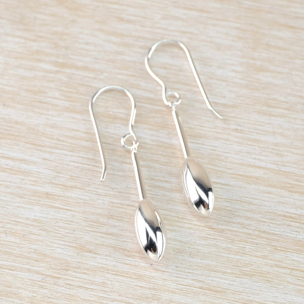 Shiny silver earrings with a 3 D pod shape at the bottom of a slim silver post, hanging from a silver hook.