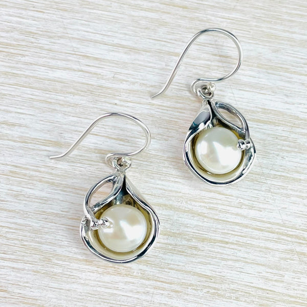 Creamy/white round pearls are nestled with a concave shaped silver teardrop with a little silver crossover at the top. Attached to a silver hook.
