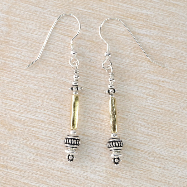 Long slender earrings with different decorated silver beads at the bottom with a long squared tube satin gold plated bead, topped with shiny silver beads. Hanging off a silver hook. 