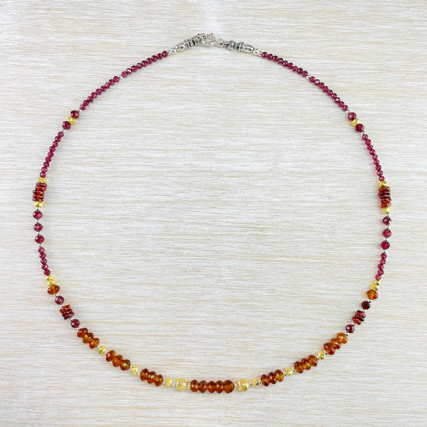 Fully beaded necklace.  At the back there are smaller faceted deep red garnet, separated by the occasional small silver bead. Half way round slightly larger red beads with gold plated beads, then a few small red beads. Towards the front there are larger beads with a slight orange tint, ingterspersed wiyh round gold plated beads. It is all symetrical and all fairly delicate beads. 