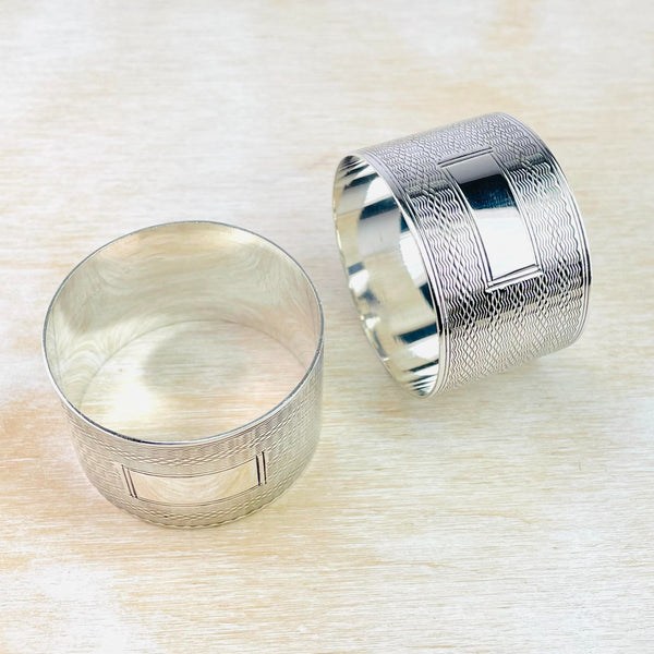 Pair of round silver napkin rings with a fine wavy  line decoration all the way around and a blankrectangular space in the middle - to engrave.dec