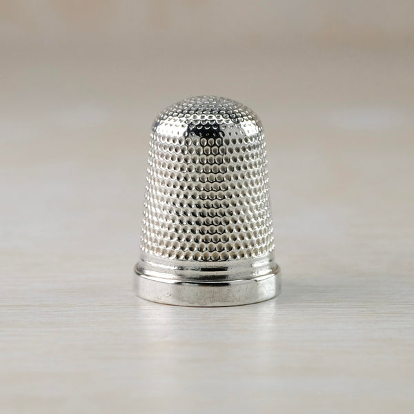 Shiny silver thimble decorated with a repeated dot indentation all over except for the high polished rim.