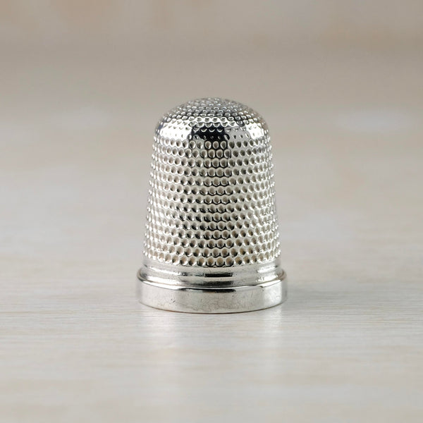 Shiny silver thimble decorated with a repeated dot indentation all over except for the high polished rim.