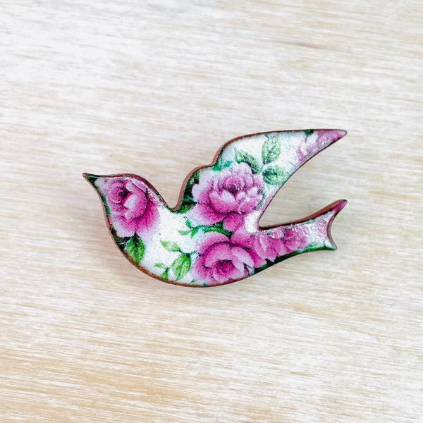 A pretty flying bird decorated with pink roses and green leaves.