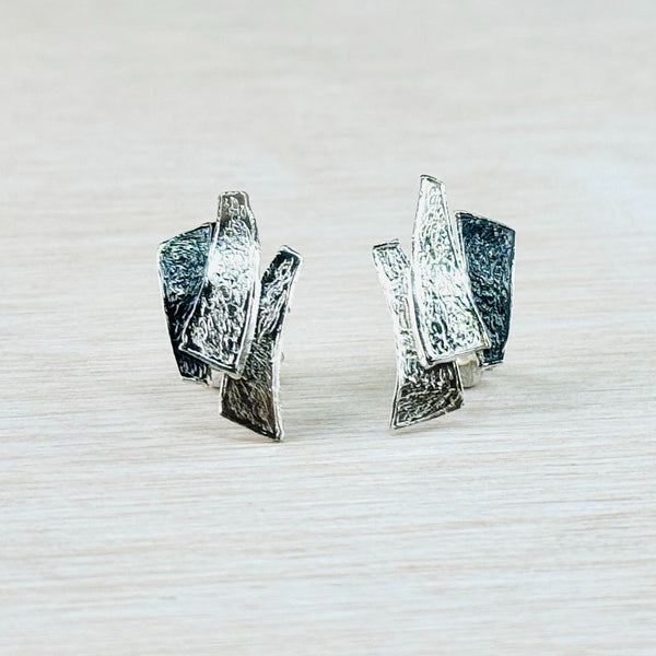 A pair of two-toned textured sterling silver stud earrings with a polished and oxidised finish, displayed against a neutral background.