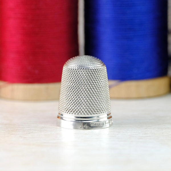 Shiny silver thimble decorated with a repeated dot indentation all over except for the high polished rim.