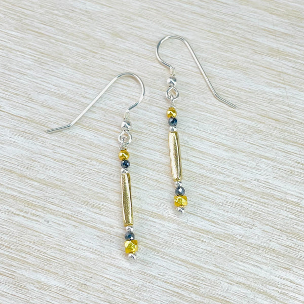 The pattern of these earrings is a small round gold bead, then a black round bead, then a matt long gold square profile bead, a silver ball, black bead and a slightly larger cut gold bead. All hanging off a silver hook.