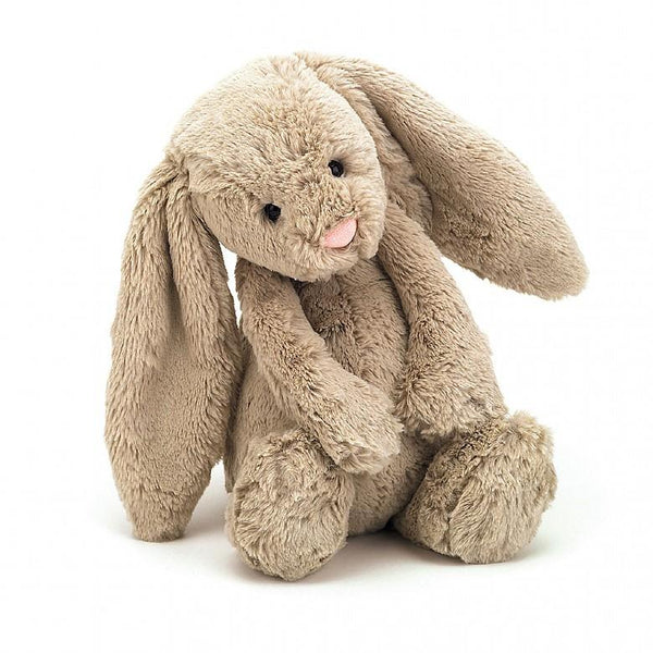 A very pretty pale beige bunny rabbit is sitting with her back legs stretched out and her front paws resting on her back feet with her head tilted to one side. She has a little rounded tummy, long soft ears, a cute pink nose and little black eyes. She looks soft and cuddly!