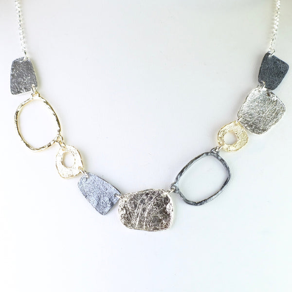 Nine different links hang off the front of this necklacet. They are all slighltly different but all vaguely rectangular. From far left is a solid oxidized shape, then a gold plated, slightly larger outline, then smaller polished silver frame, then oxidized silver solid rectangle, then textured silver, oxidized silver outline, shiny textured smaller frame,  solid textured silver and finallu oxidized solid silver to match the first one.