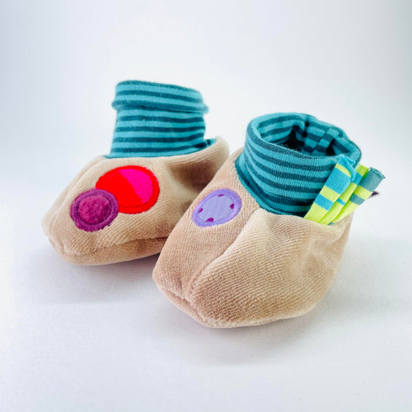 Bootie style slippers with the bottom half in beige  and the top, a blue horizontal stirpe elasticated 'sock'. On the right hand slipper there are two large dots, one orange and a smaller purple one slightly overlapping that. The left hand slipper has a single pale purple dot.