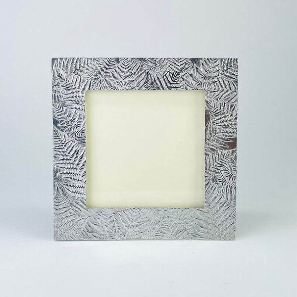A square pewter photo frame with a fern leaf design arranged around the frame in a random form. 
