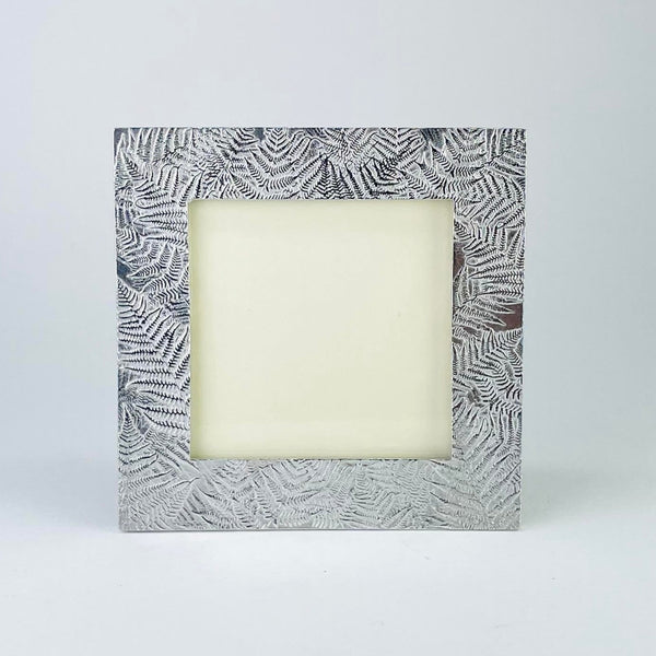 A square pewter photo frame with a fern leaf design arranged around the frame in a random form. 
