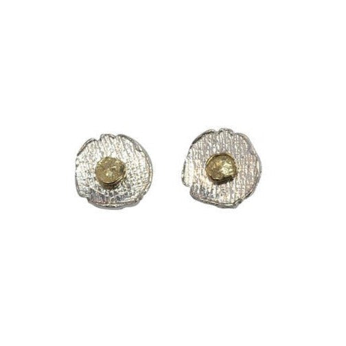 The stud earrings have an overall round shape, but the outline is slightly wavy with little inward notches. The silver is textured with a a gentle striped effect. In the centre of the circle is a textured gold coloured circle, also not perfectly circular, which sits on top of the silver one, 