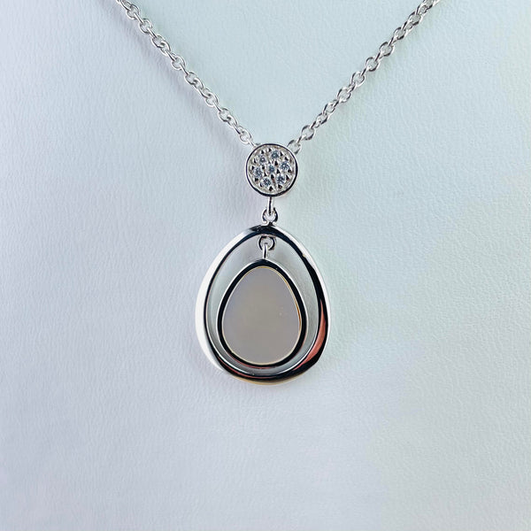 A pendant formed of twp pieces. The top piece is a silver circle studded with seven sparkly cubic zirconia stones. The bottom part, much bigger, is a soft tear drop shape, itself in two parts. The outer part is shiny silver with a smaller tear drop mother of pearl hanging inside, connected at the top