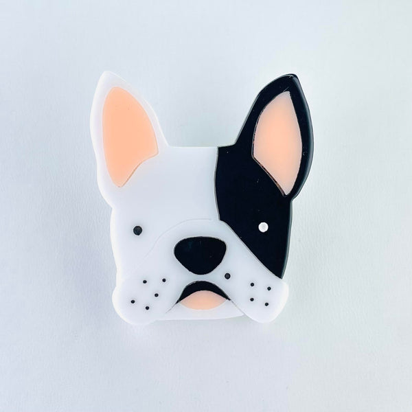 The cutest face of a French Bulldog looking straight on. One third of the face is black, from just below the eye to the tip of the ear, the rest is white. It has a black nose, black freckles and a black top lip. A little pink tongue is showing and the inside of both ears is pink.